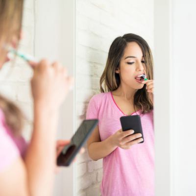 Woman brushing teeth while looking at her phone